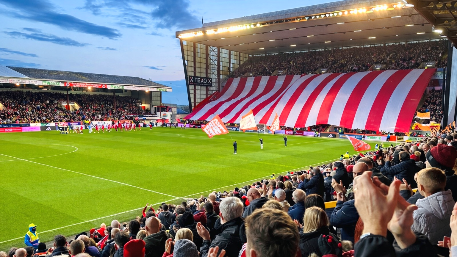 A packed football stadium with a giant red and white striped banner across the stands.