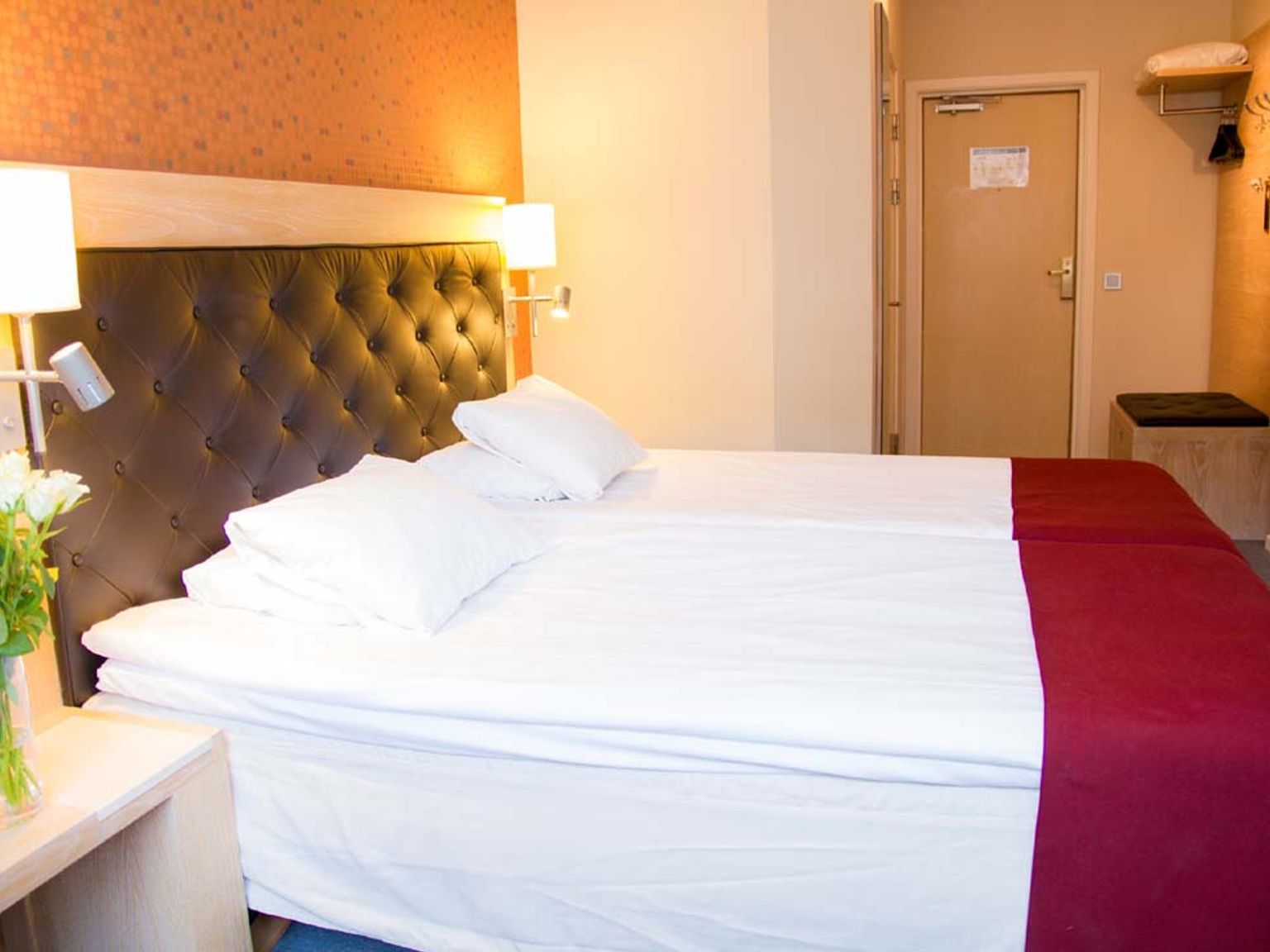 et hotelværelse med to senge og en vase med blomster på natbordet