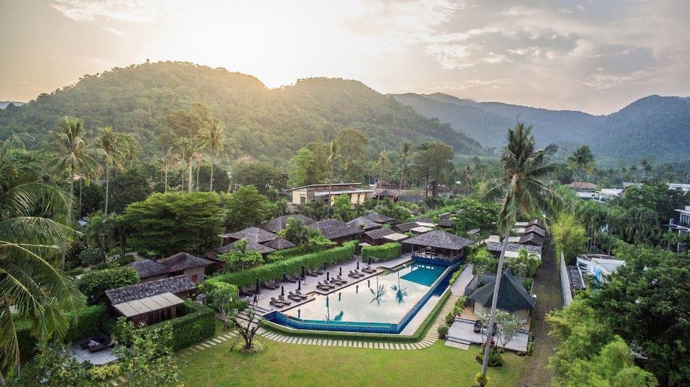 eine Luftaufnahme eines tropischen Resorts mit einem großen Swimmingpool, umgeben von Palmen und Bergen.