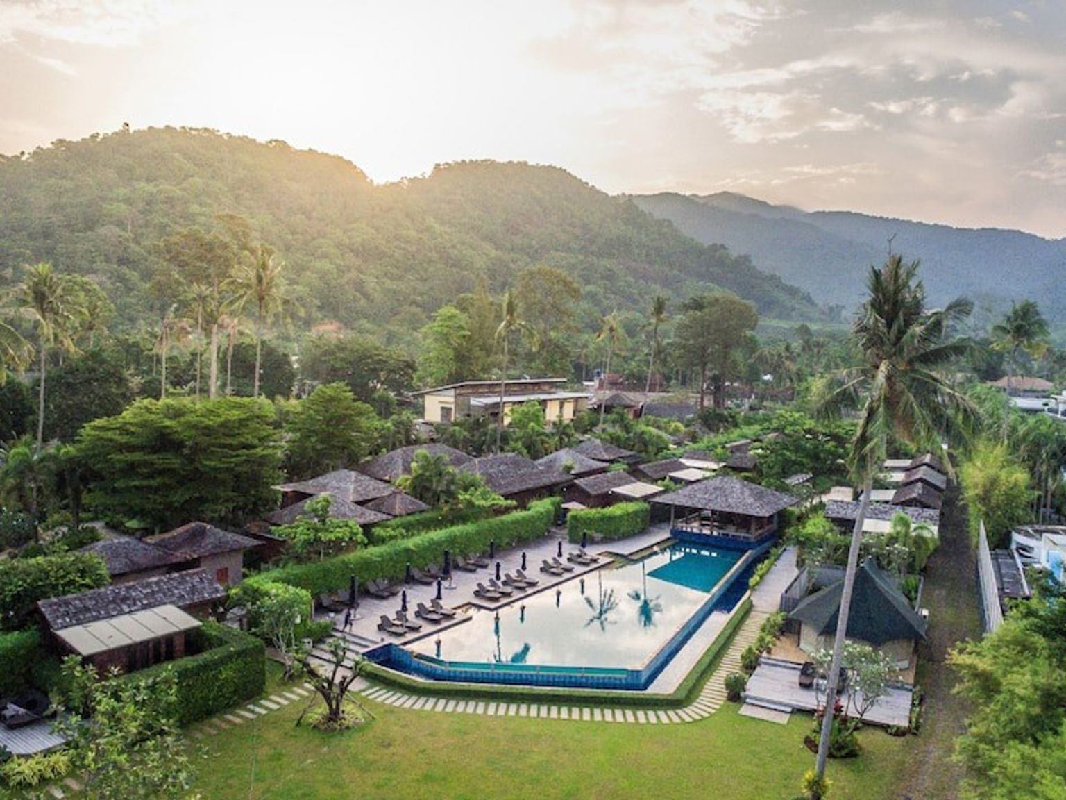 eine Luftaufnahme eines tropischen Resorts mit einem großen Swimmingpool, umgeben von Palmen und Bergen.