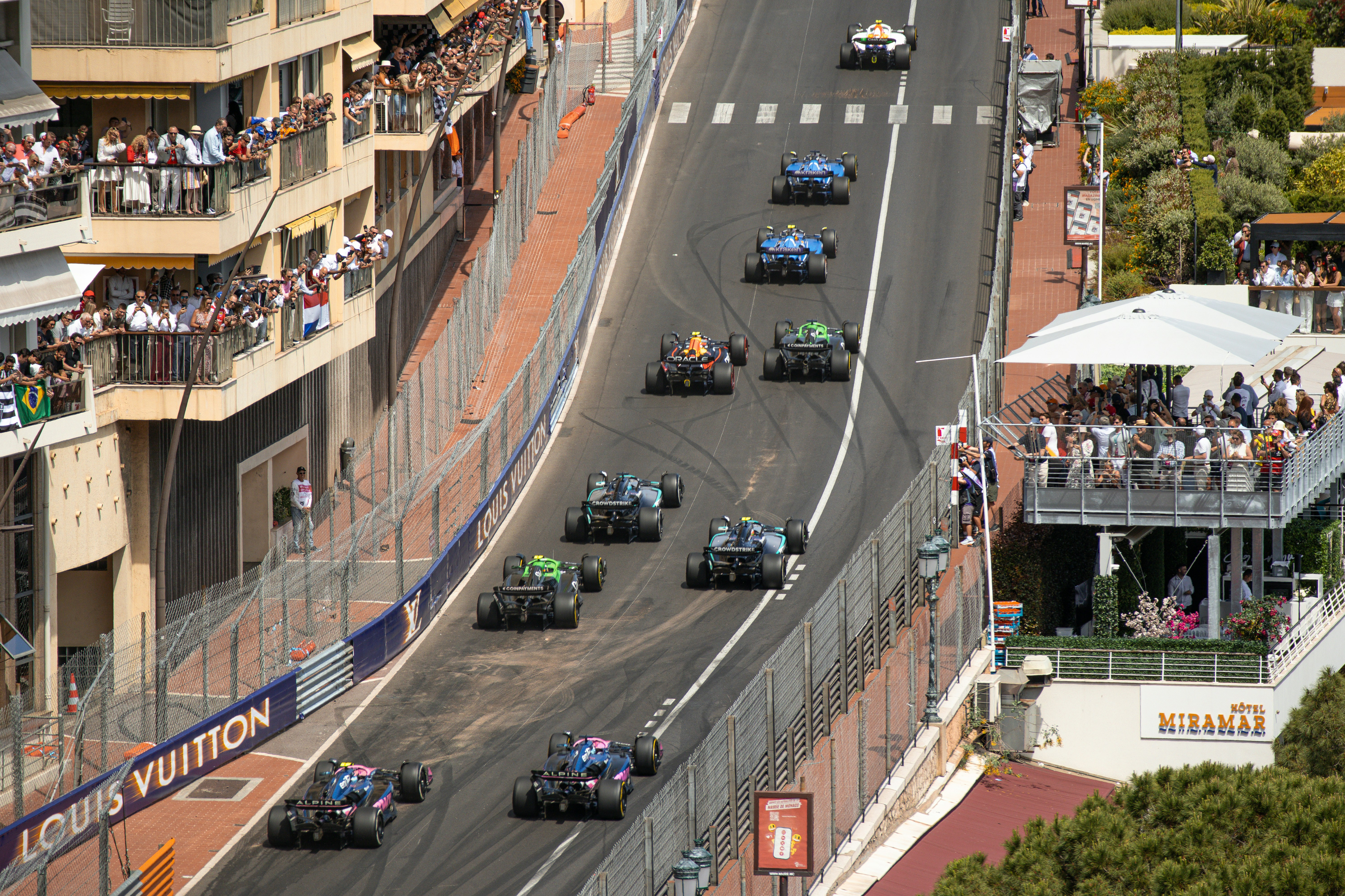 Overhead view of Formula race cars on a street circuit lined with spectators.