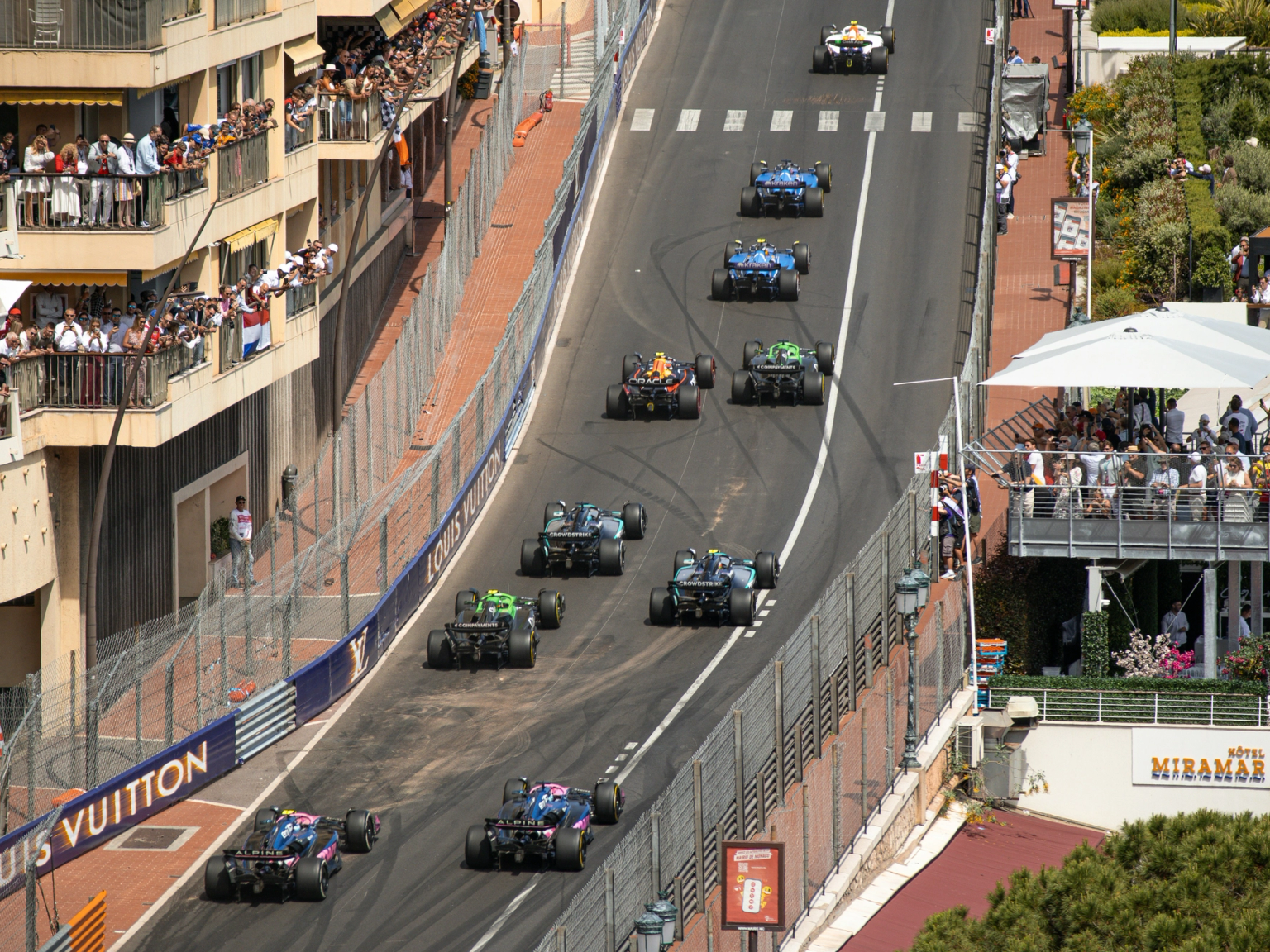 Overhead view of Formula race cars on a street circuit lined with spectators.