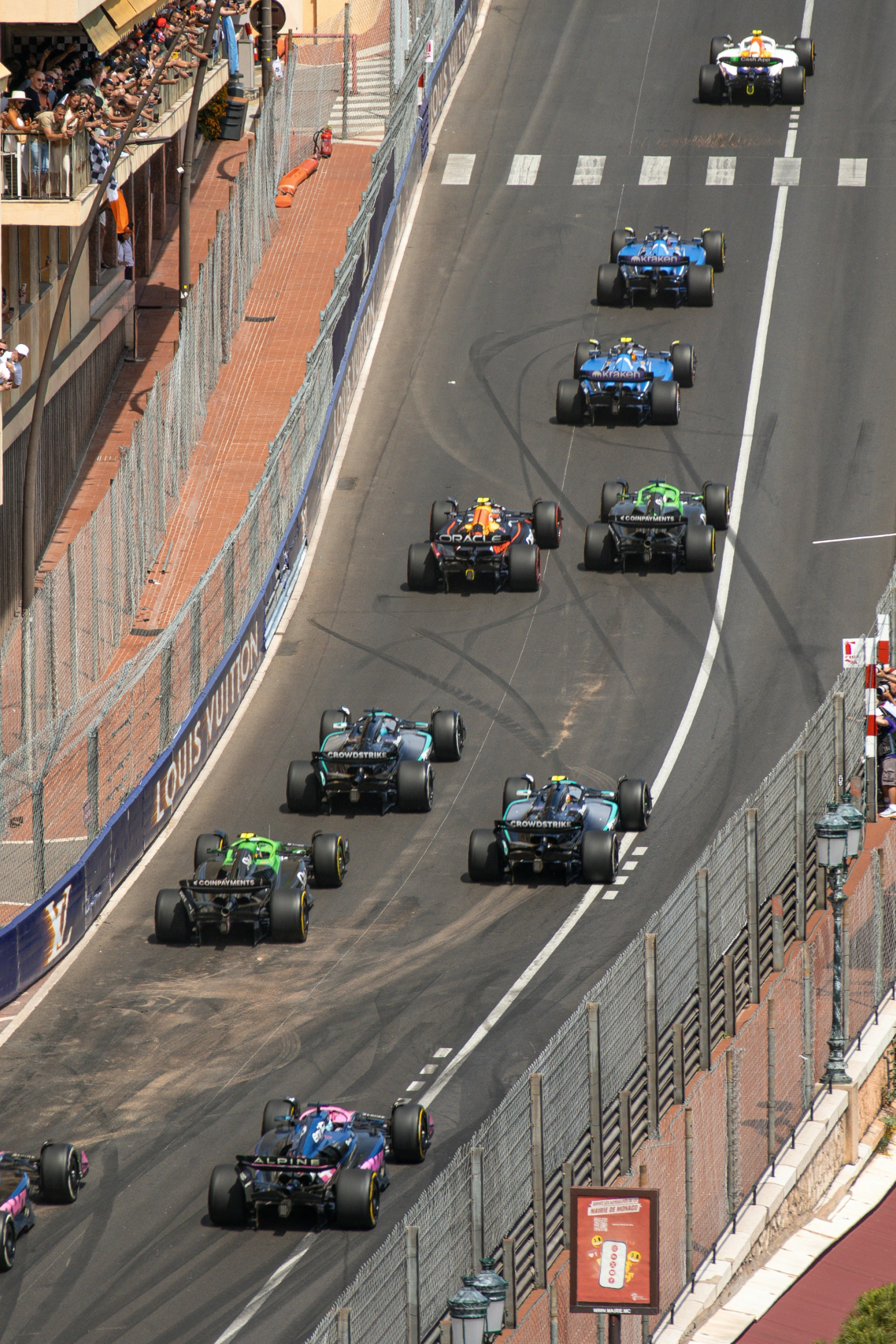 Overhead view of Formula race cars on a street circuit lined with spectators.