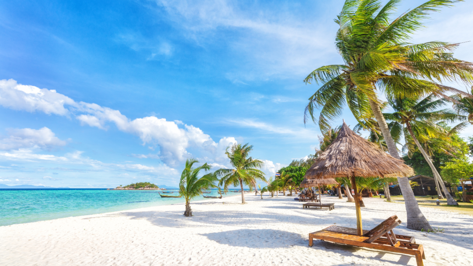 White sand tropical beach with palm trees, turquoise ocean, and a straw umbrella with lounge chairs.
