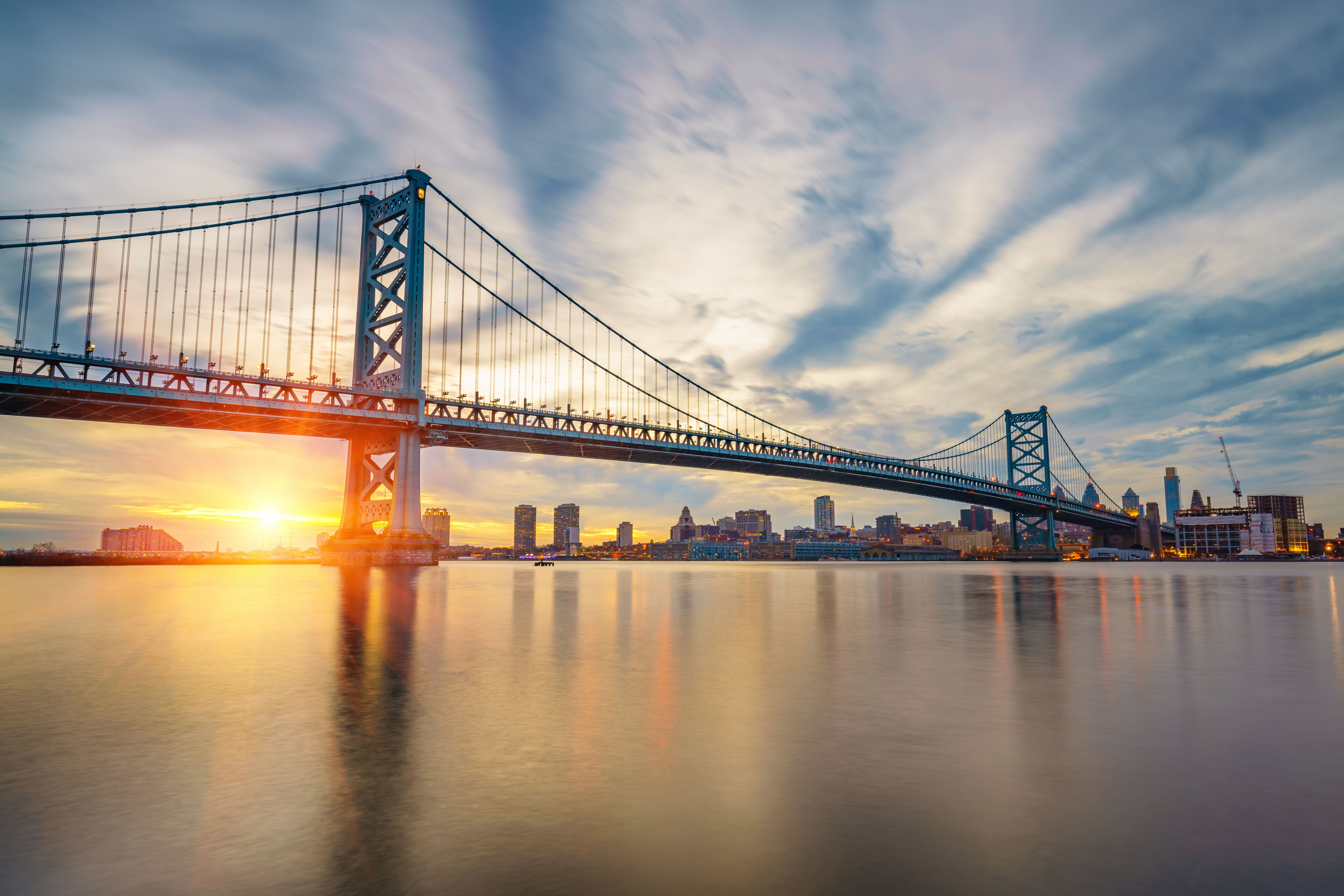 Benjamin Franklin-broen ved solnedgang over vandet med Philadelphias skyline.