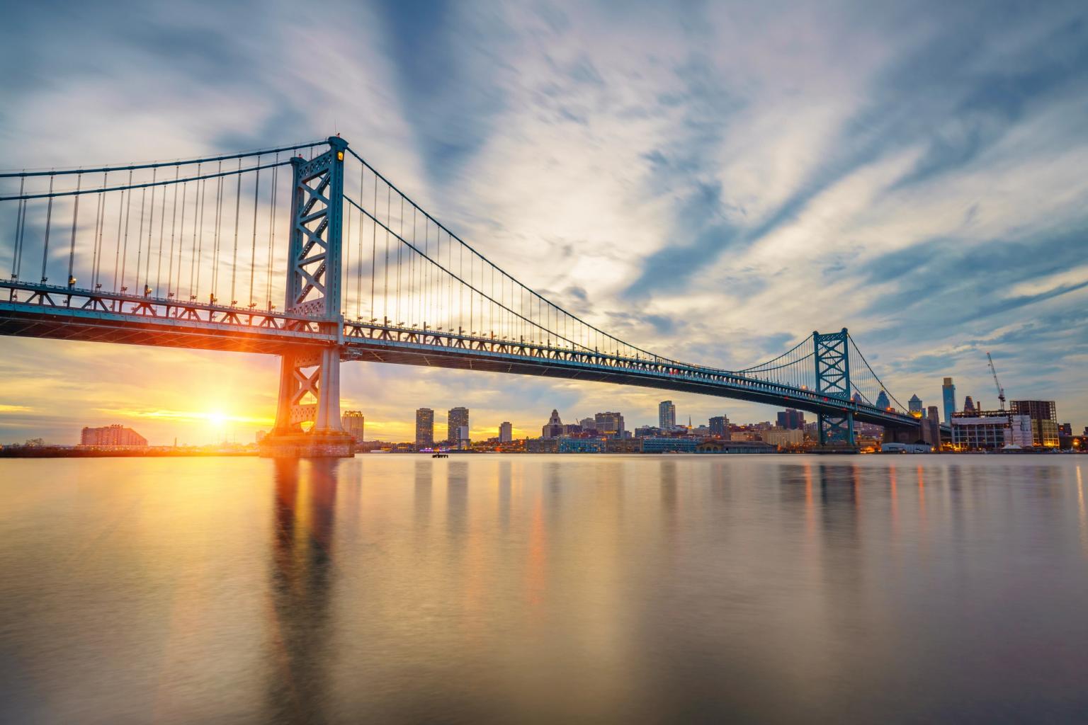 Benjamin Franklin-broen ved solnedgang over vandet med Philadelphias skyline.