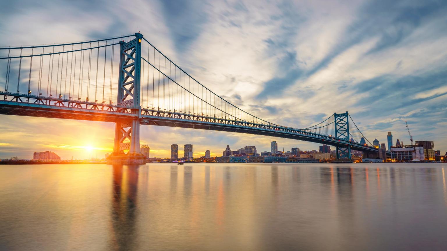 Benjamin Franklin-broen ved solnedgang over vandet med Philadelphias skyline.