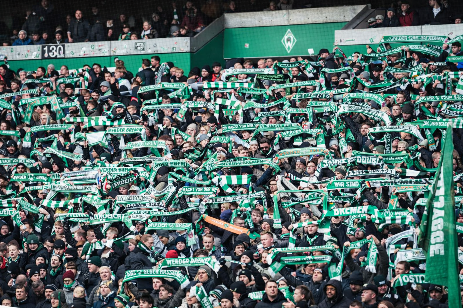 Aficionados en un estadio sosteniendo bufandas verdes y blancas.