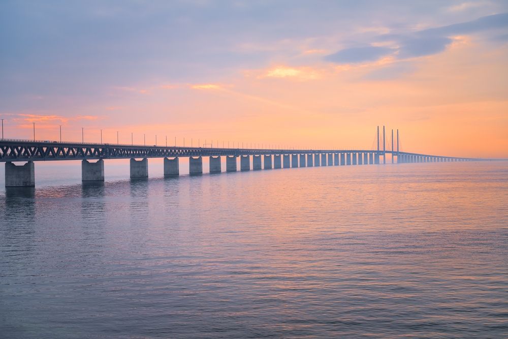 Öresundsbron sträcker sig över stilla vatten under en färgstark soluppgångshimmel och visar både sina viadukt- och snedkabelsektioner.