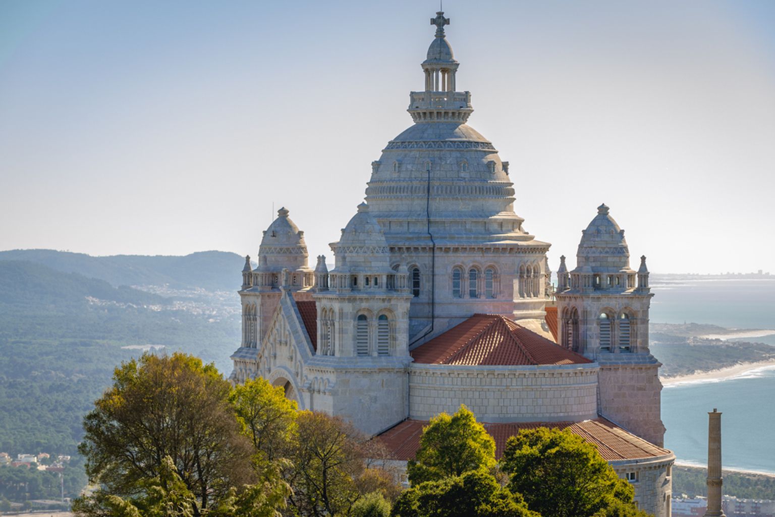 En majestätisk basilika i vit sten med en kupol och torn, belägen på en kulle ovanför bergen och havet.