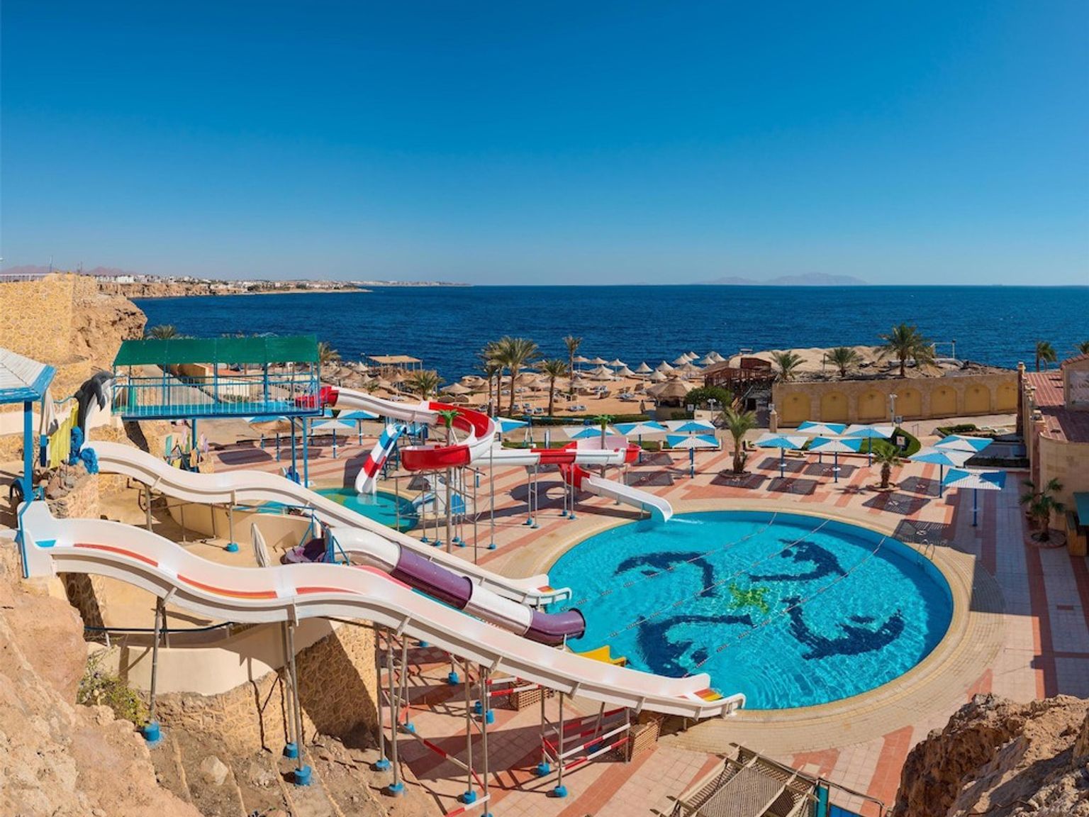 Vattenpark med flera rutschkanor och en pool med utsikt över havet och en sandstrand.