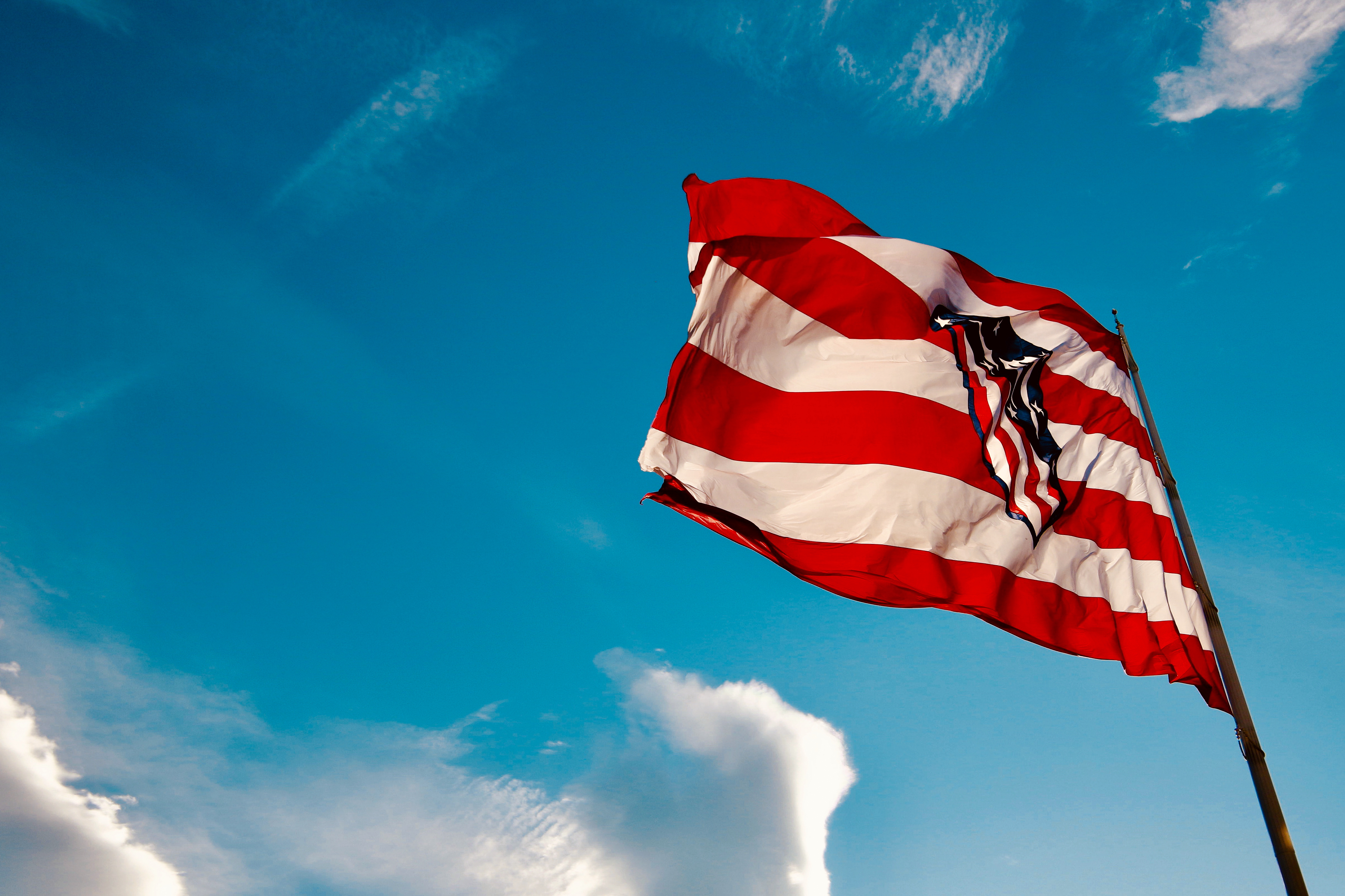 Bandera del Atlético de Madrid con rayas rojas y blancas ondeando contra un cielo azul brillante.