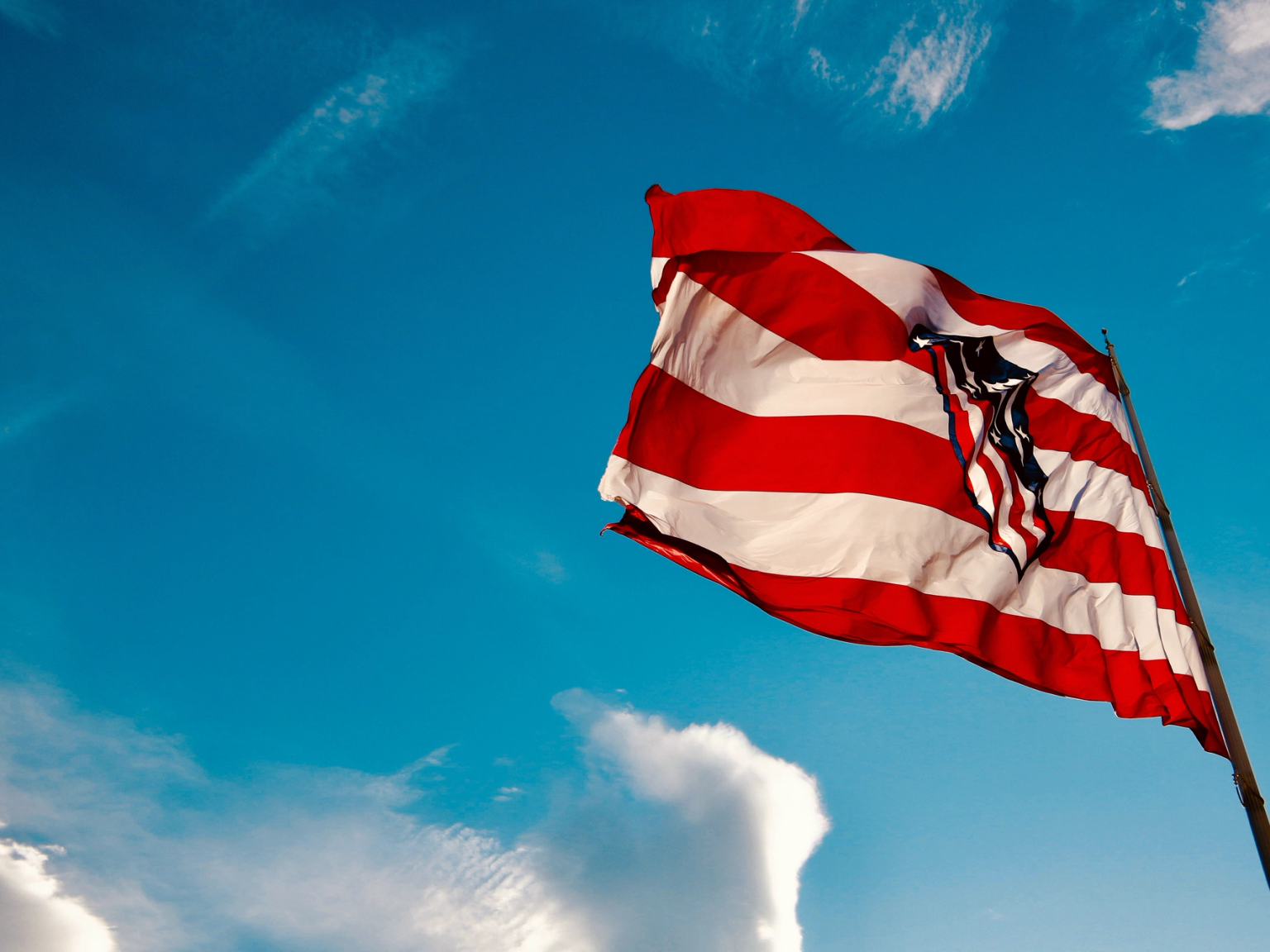 Atlético Madrid-flag med røde og hvide striber, der vajer mod en klar blå himmel.
