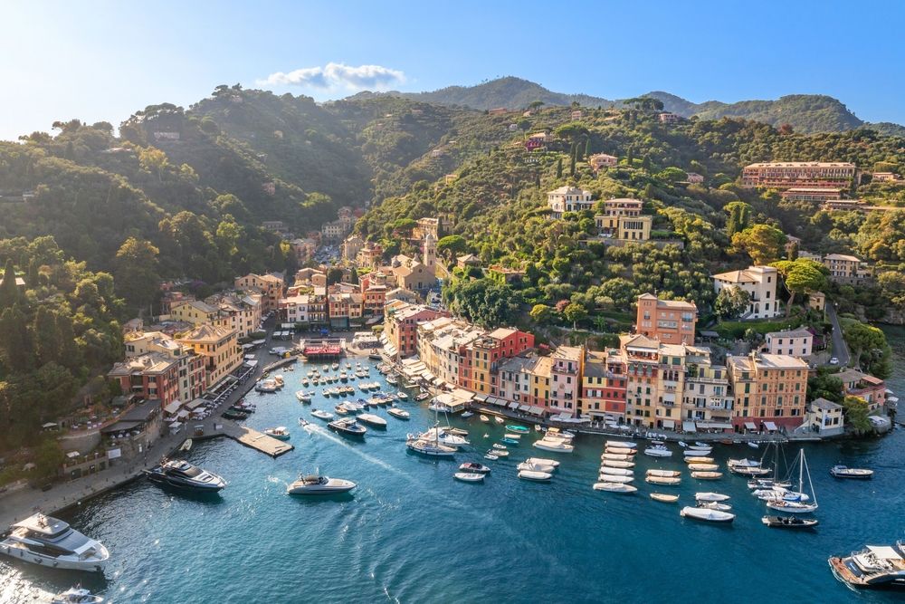 Luftfoto af en farverig kystby med en havn fyldt med både og grønne bakker. Portofino, Italien