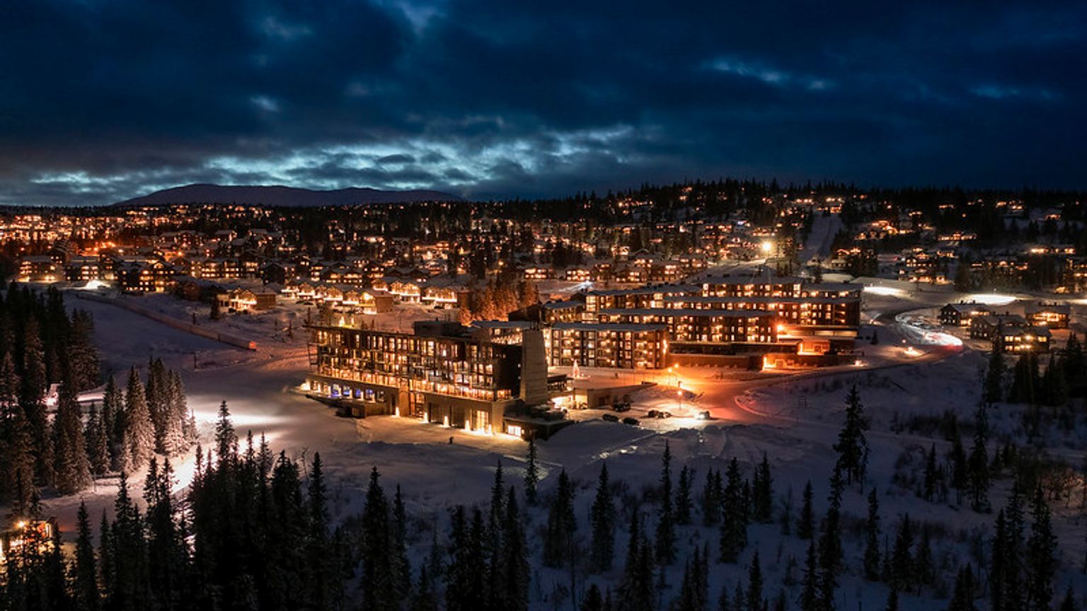 et luftfoto af et skisportssted om natten omgivet af sneklædte træer.