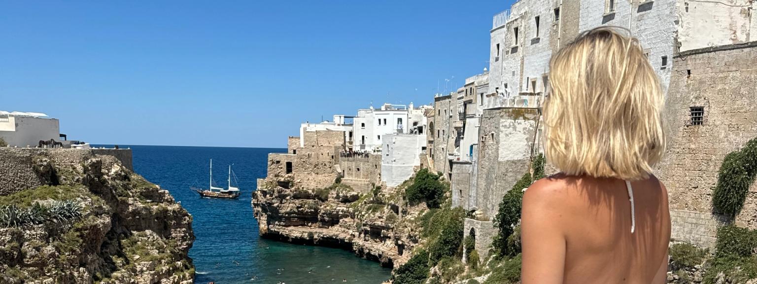 en kvinna i en vit klänning står på en balkong med utsikt över en strand