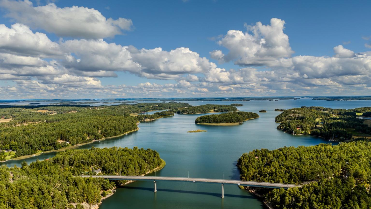 Luftfoto af en skovklædt øgruppe med en bro over blåt vand under en overskyet himmel.