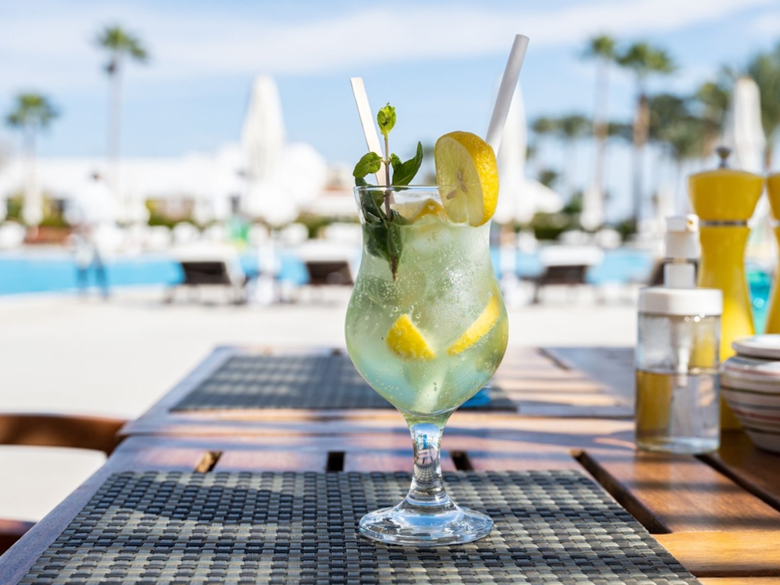 Ein erfrischendes Zitronen-Minze-Getränk mit einem Strohhalm auf einem Tisch an einem sonnigen Swimmingpool.