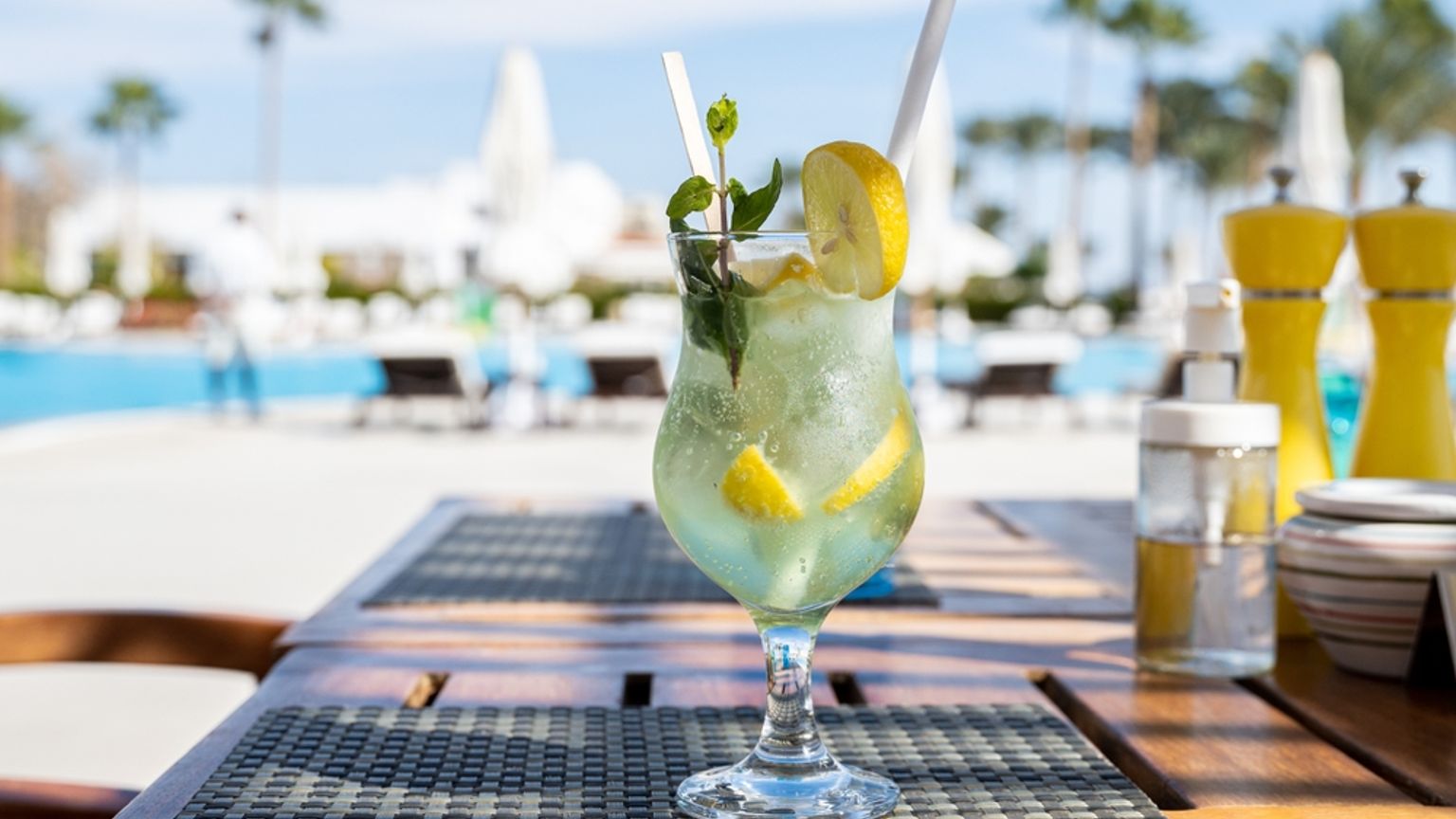 En forfriskende sitron- og myntedrikk med et sugerÞr pÄ et bord ved et solfylt svÞmmebasseng.