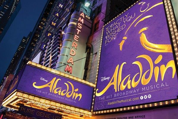 Vue nocturne du New Amsterdam Theatre, brillamment illuminé par des enseignes violettes et dorées pour Aladdin de Disney.