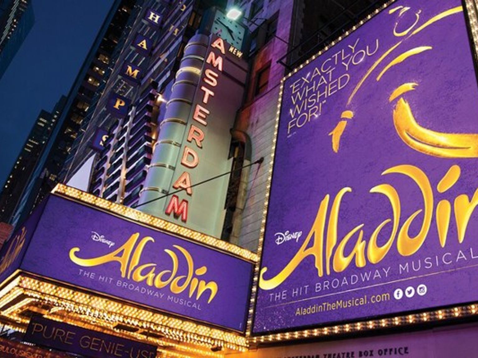 Vue nocturne du New Amsterdam Theatre, brillamment illuminé par des enseignes violettes et dorées pour Aladdin de Disney.