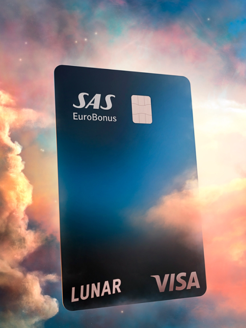 Et Lunar SAS EuroBonus Visa-kort, der svæver blandt farverige, drømmeagtige skyer under en stjerneklar nattehimmel.