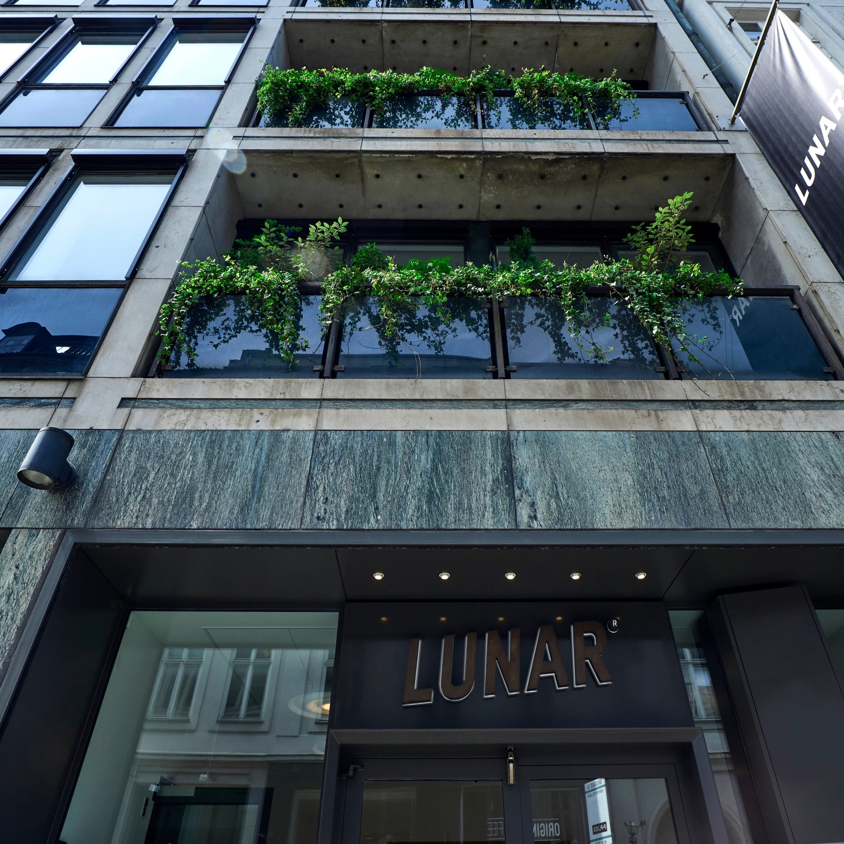 En gatuvy från en låg vinkel av ingången till den moderna Lunar-kontorsbyggnaden, som visar företagets logotyp ovanför dörrarna och på en stor banderoll.
