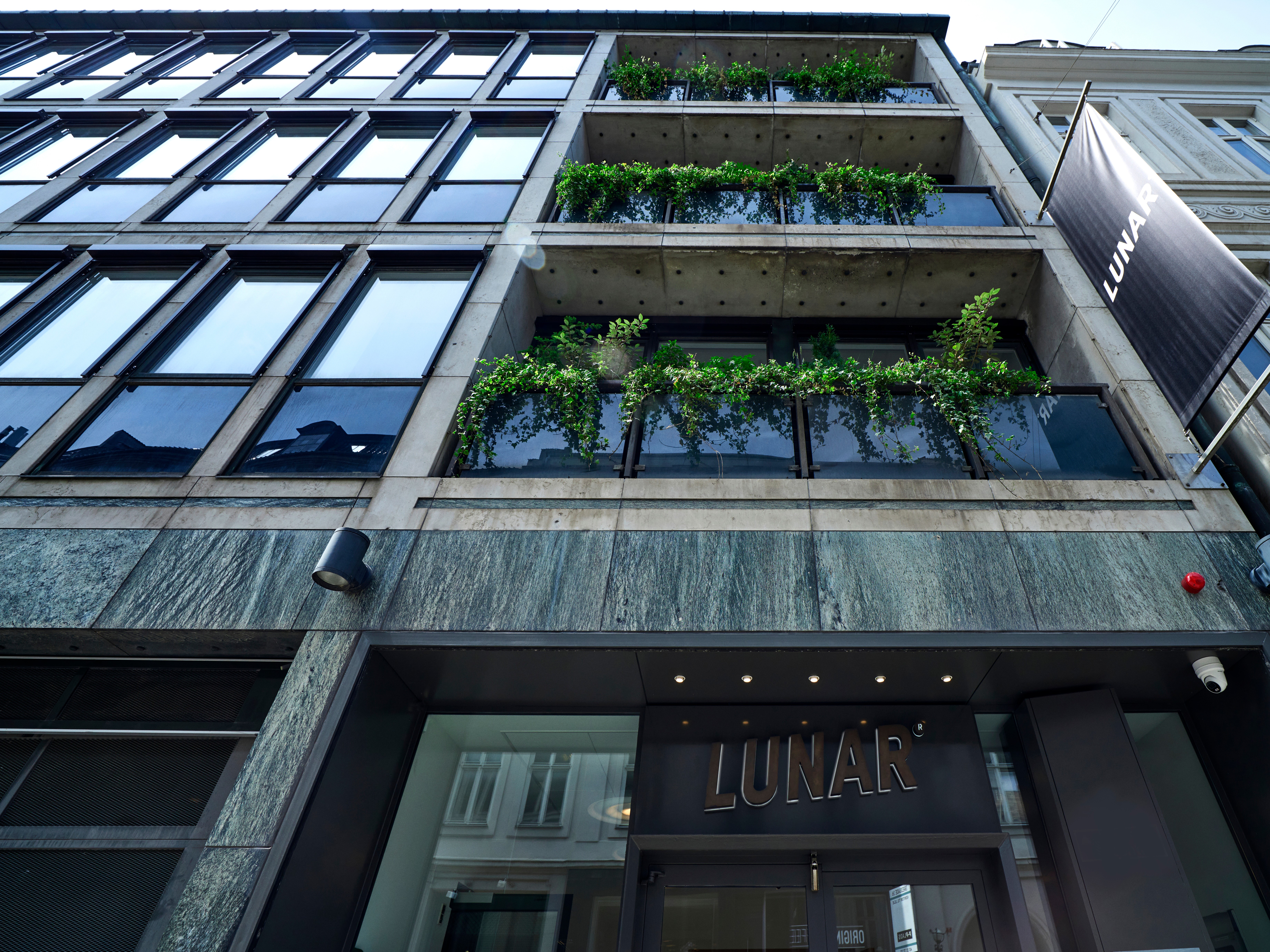 A low-angle street view of the modern Lunar office building entrance, showing the company logo above the doors and on a large banner.