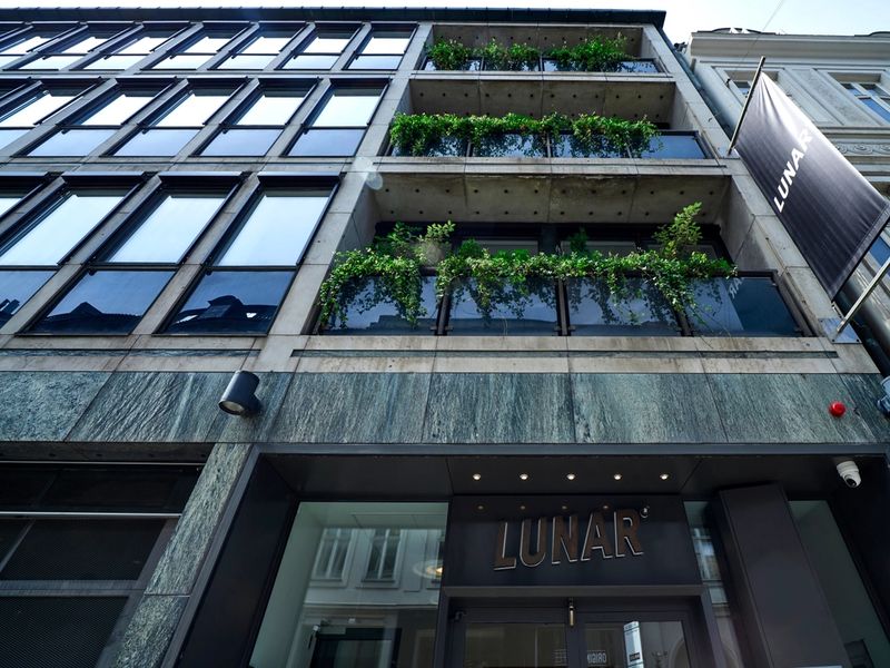 A low-angle street view of the modern Lunar office building entrance, showing the company logo above the doors and on a large banner.