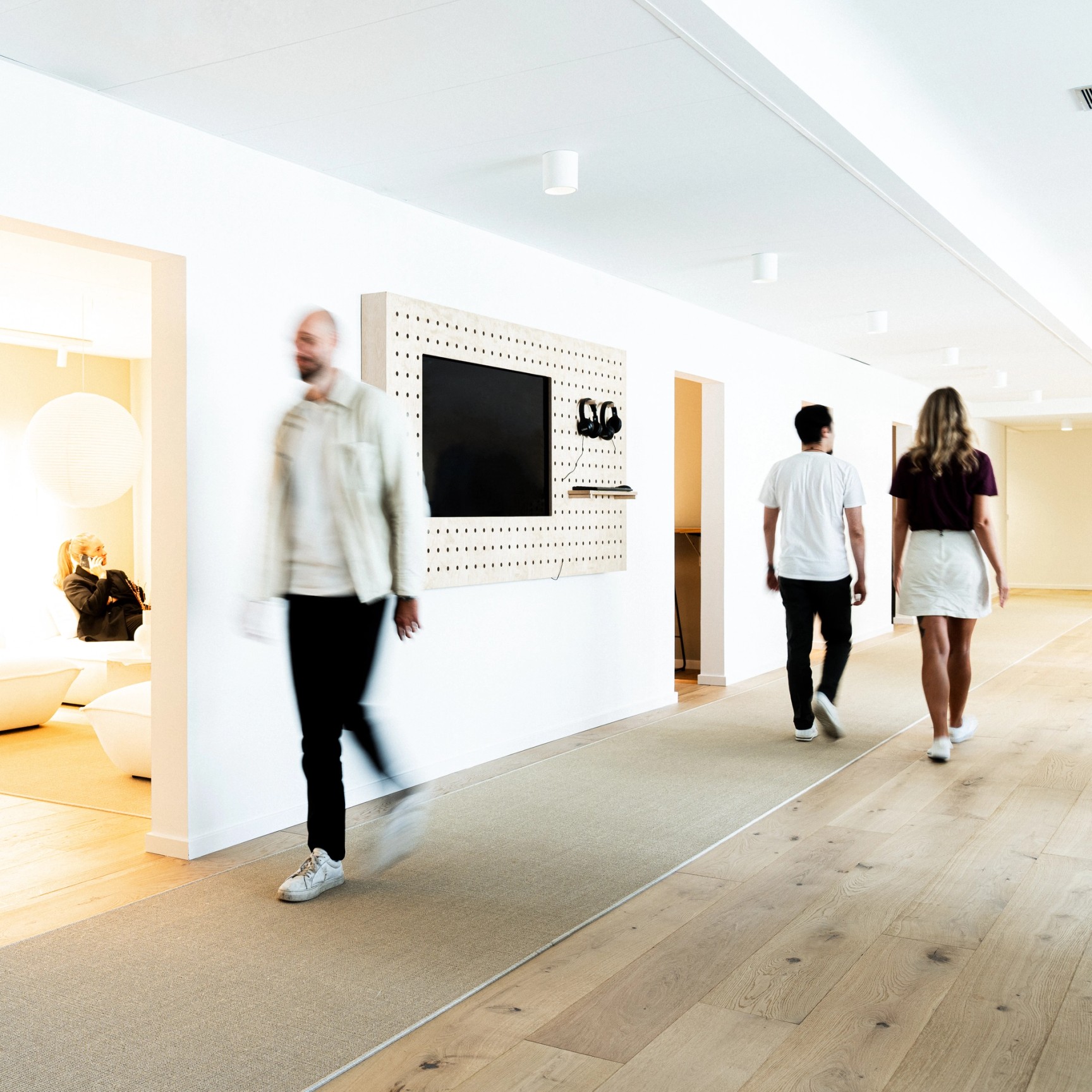 En ljus, modern kontorskorridor med flera personer som går igenom den. En man i förgrunden är suddig av rörelse, vilket skapar en dynamisk känsla av en livlig arbetsplats.