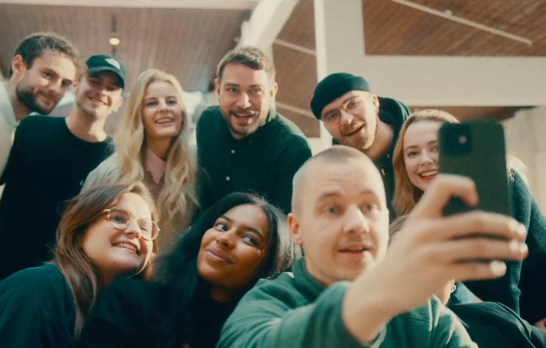 En stor, mångfaldig grupp unga människor som tränger ihop sig, ler och skrattar medan de tar en gruppselfie.