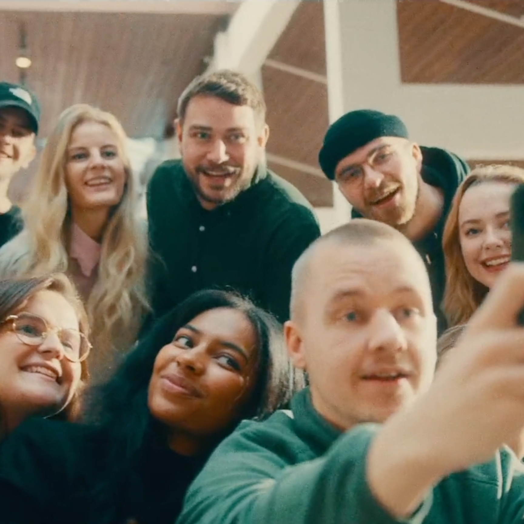 En stor, mångfaldig grupp unga människor som tränger ihop sig, ler och skrattar medan de tar en gruppselfie.