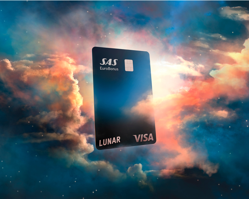 Et Lunar SAS EuroBonus Visa-kort, der svæver blandt farverige, drømmeagtige skyer under en stjerneklar nattehimmel.