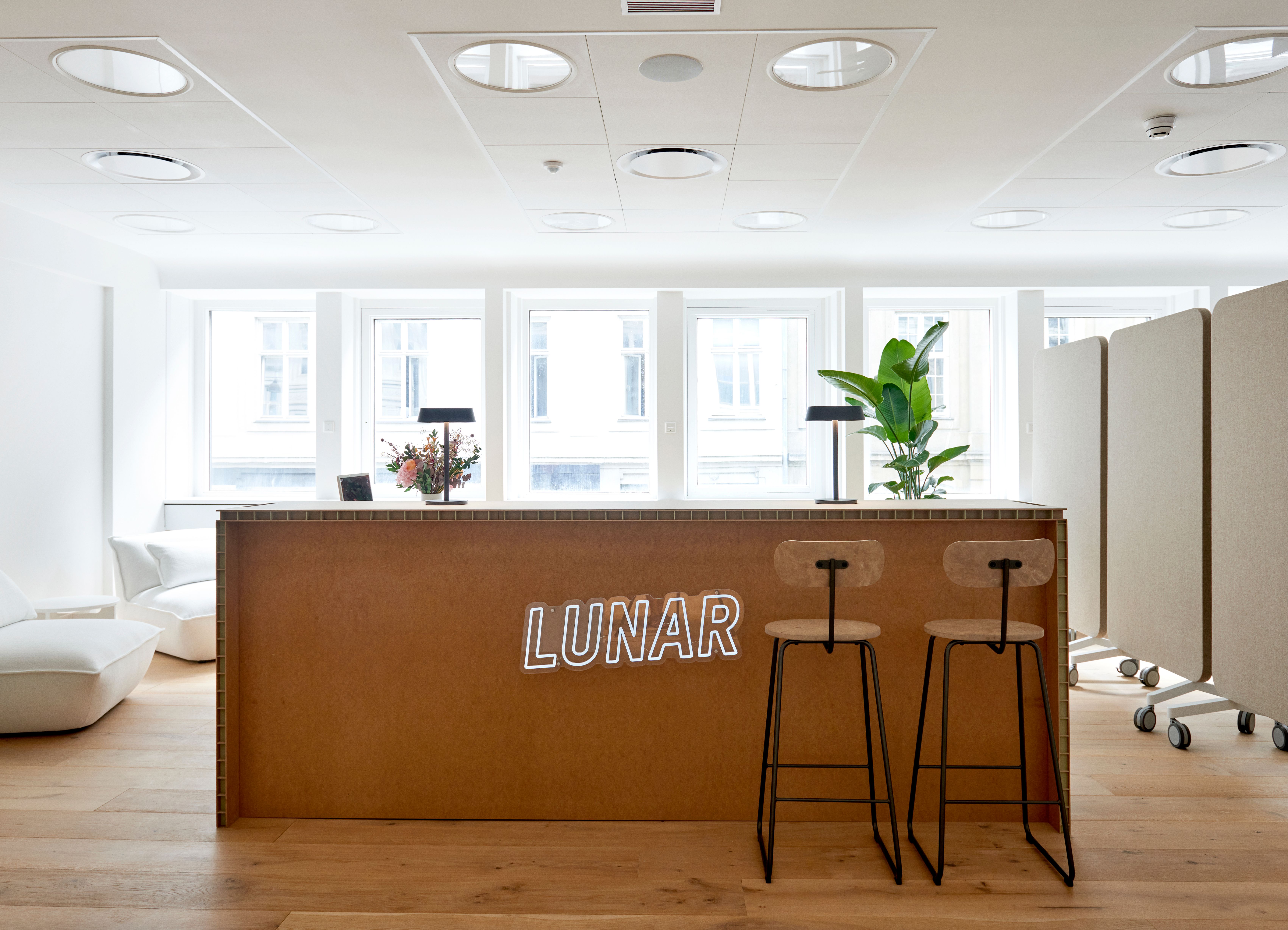 The modern and bright reception area of the Lunar office, featuring a wooden desk with a white neon "LUNAR" sign on the front.