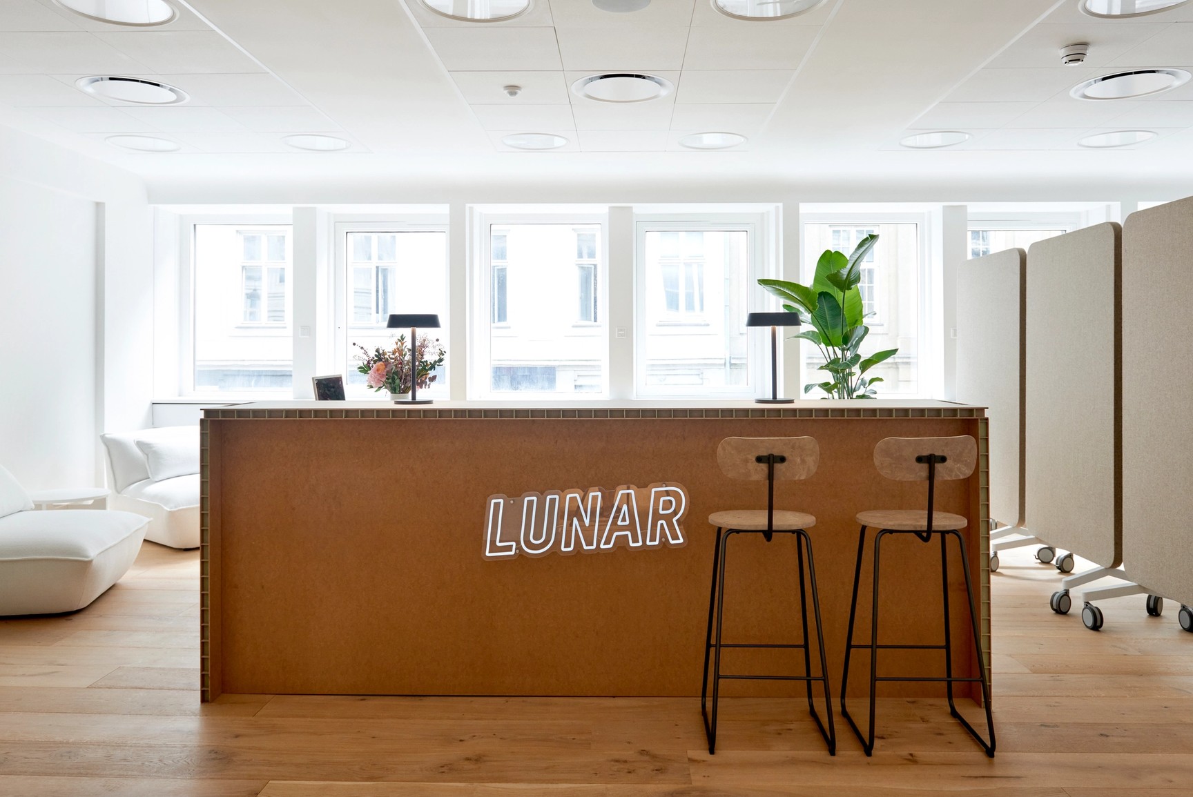 Det moderna och ljusa receptionsområdet på Lunar-kontoret, med en trädisk som har en vit "LUNAR"-neonskylt på framsidan.