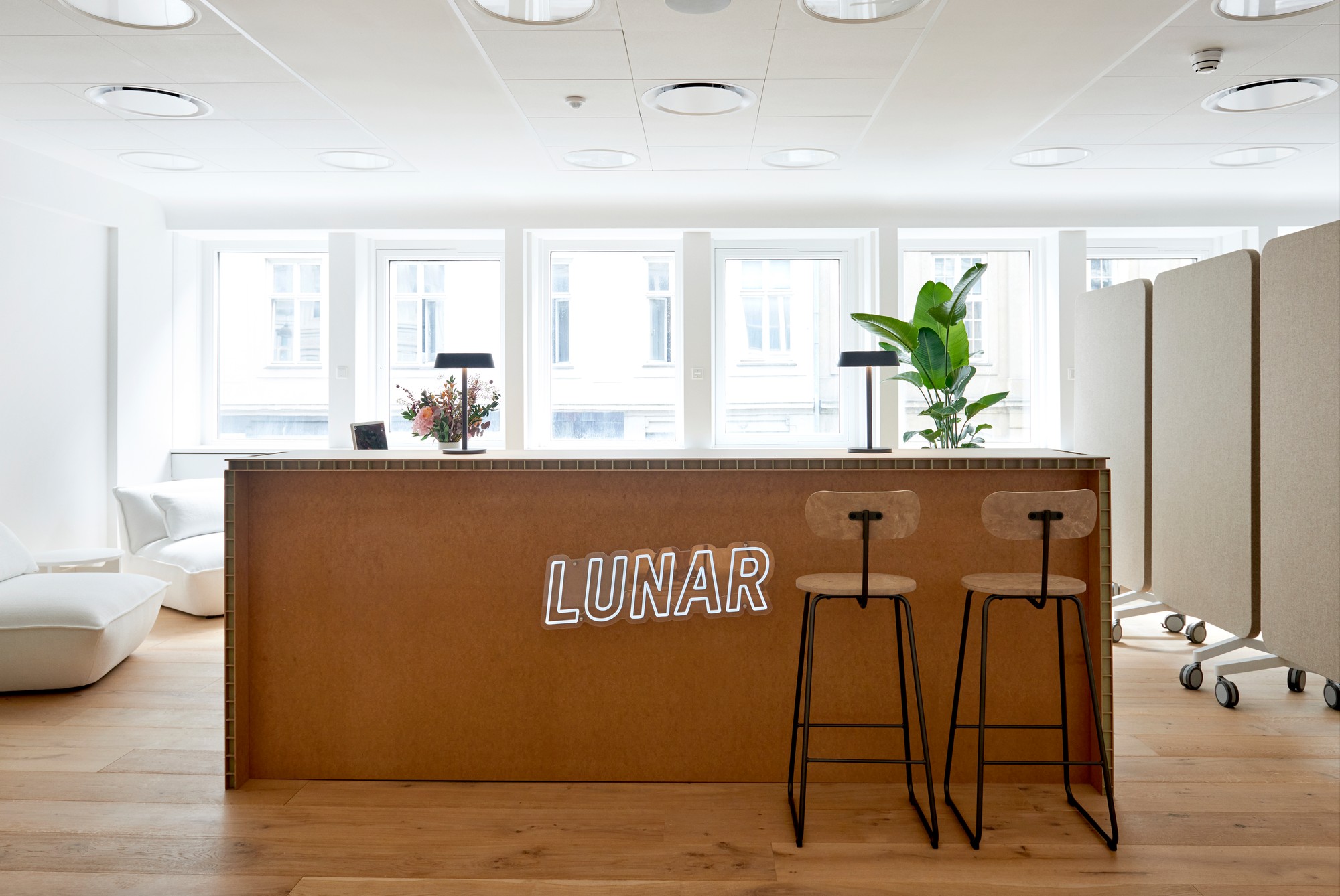 Det moderna och ljusa receptionsområdet på Lunar-kontoret, med en trädisk som har en vit "LUNAR"-neonskylt på framsidan.
