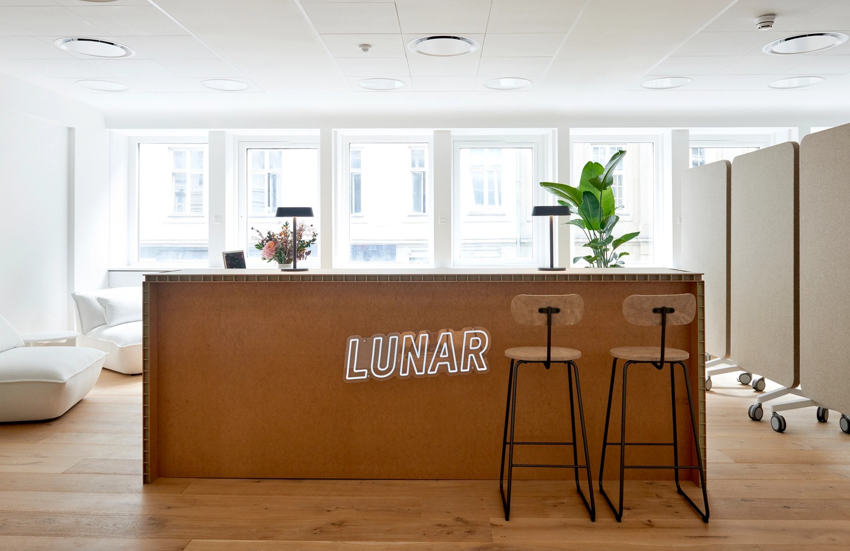 Det moderne og lyse receptionsområde på Lunar-kontoret, som har en træskranke med et hvidt "LUNAR"-neonskilt på forsiden.