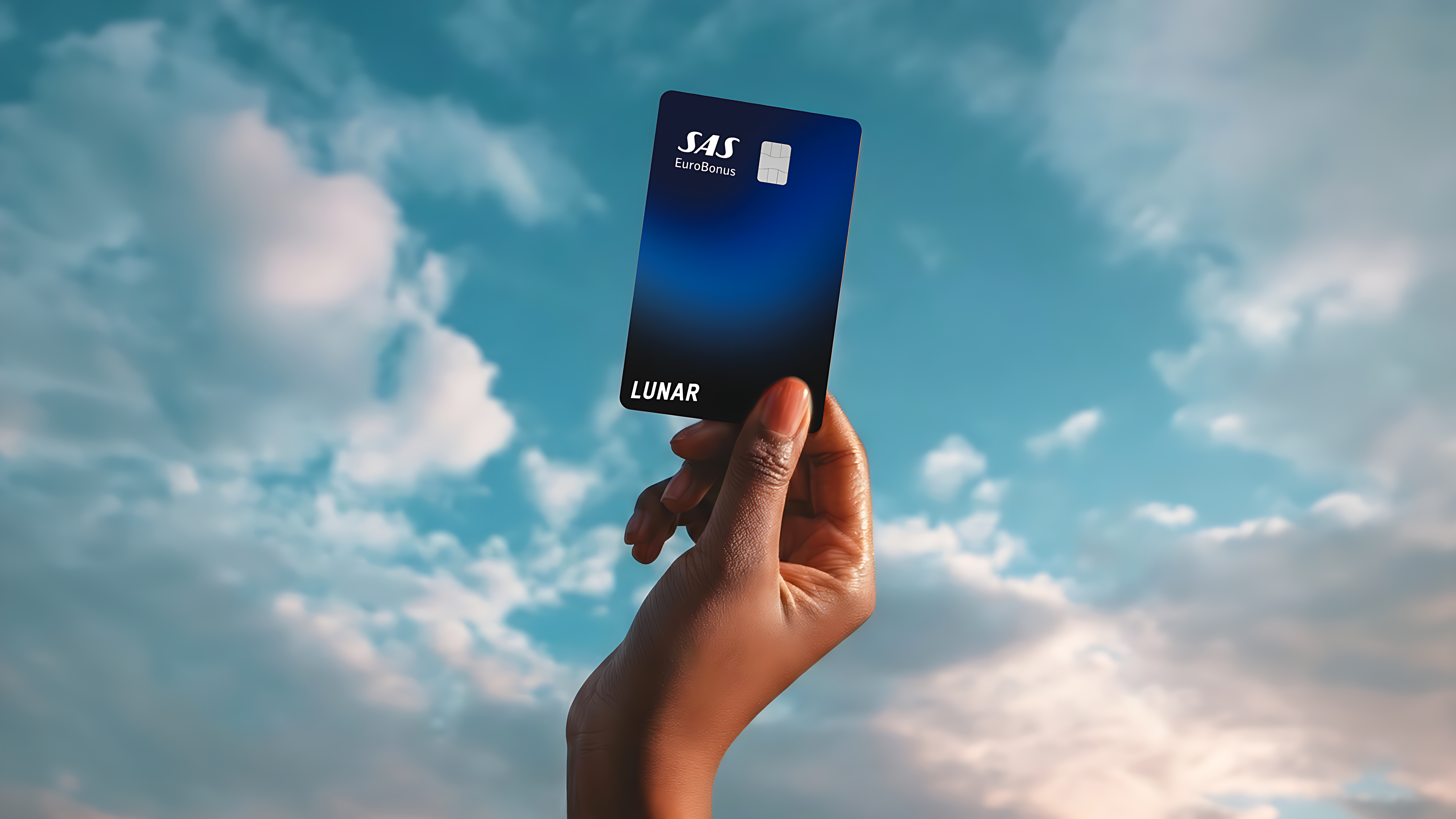 Lunar SAS EuroBonus Visa-kortet, der svæver horisontalt blandt farverige, drømmeagtige skyer under en stjernehimmel.