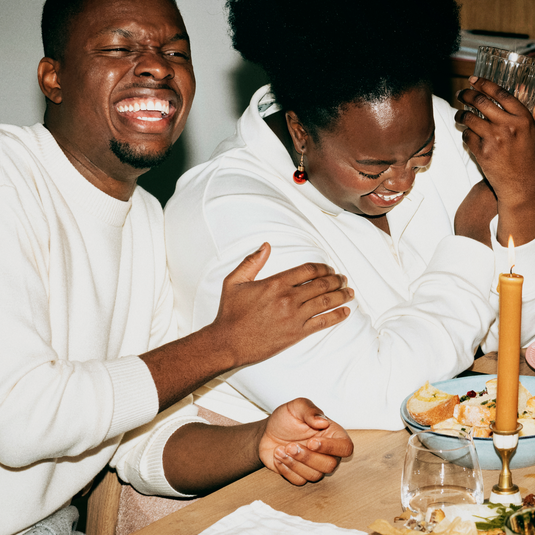 En man och en kvinna skrattar hjärtligt tillsammans vid ett middagsbord med tända ljus, vilket skapar en varm och glad atmosfär.