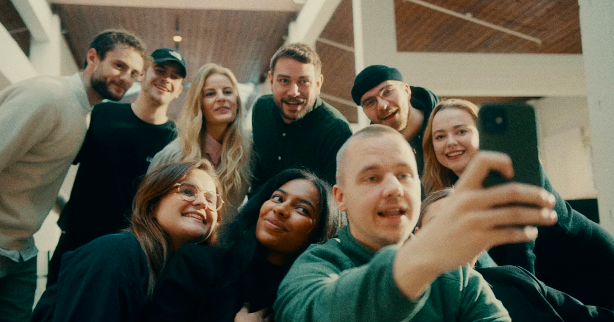 En stor, mangfoldig gruppe unge mennesker, der er samlet tæt sammen, smiler og griner, mens de tager en gruppeselfie.