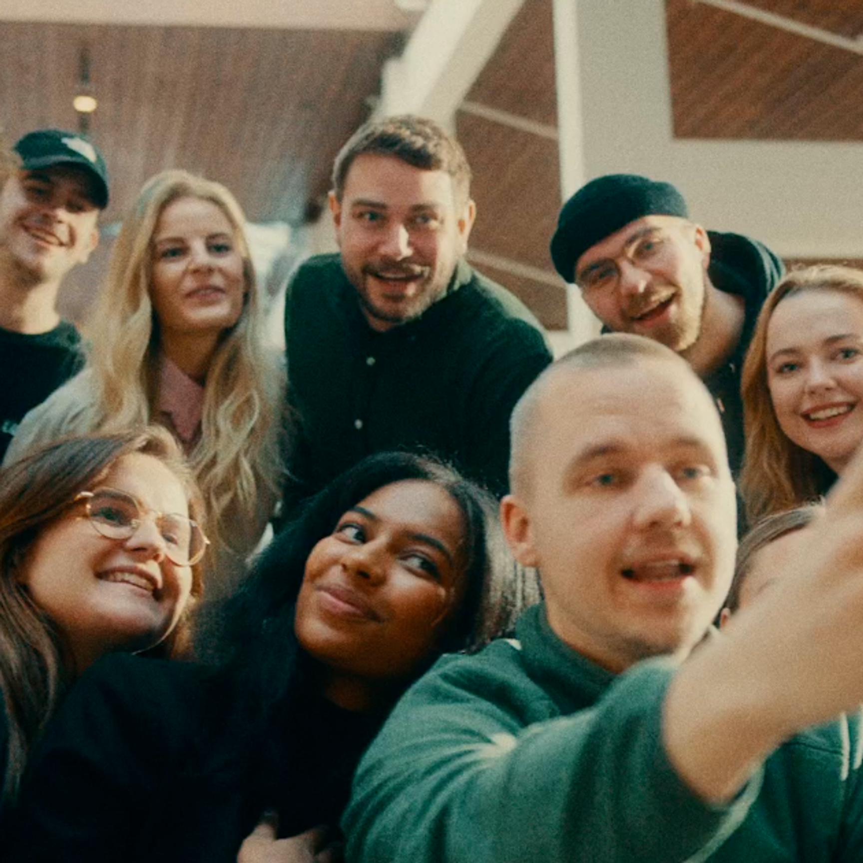 En stor, mangfoldig gruppe unge mennesker som er trengt sammen, smiler og ler mens de tar en gruppeselfie.