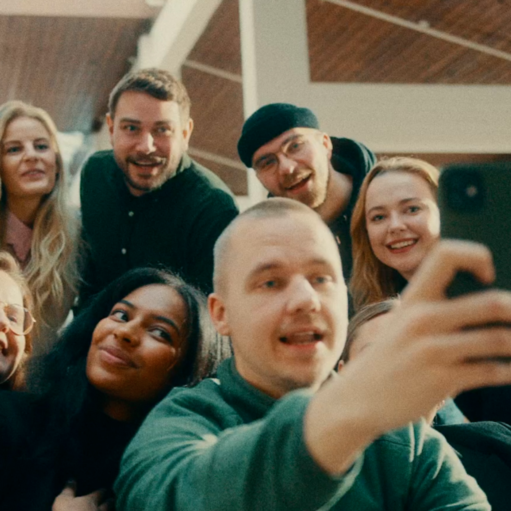 En stor, mangfoldig gruppe unge mennesker, der er samlet tæt sammen, smiler og griner, mens de tager en gruppeselfie.