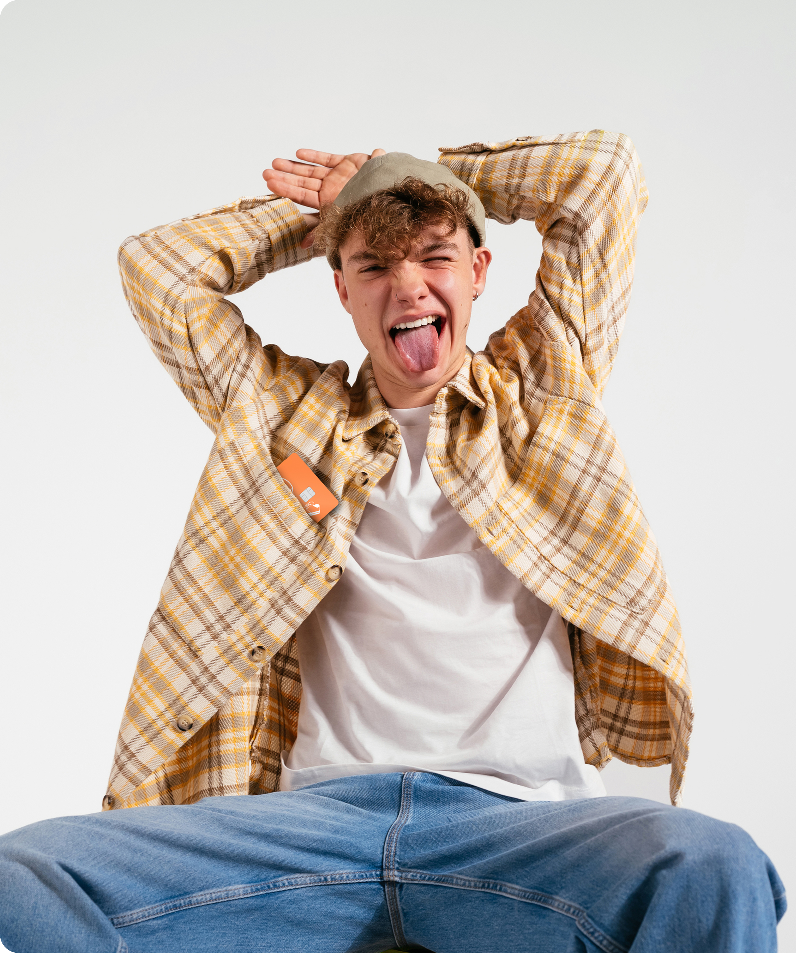  En tenåring i en gulrutete skjorte og lue lager en leken grimase og rekker tunge til kameraet med hendene bak hodet.