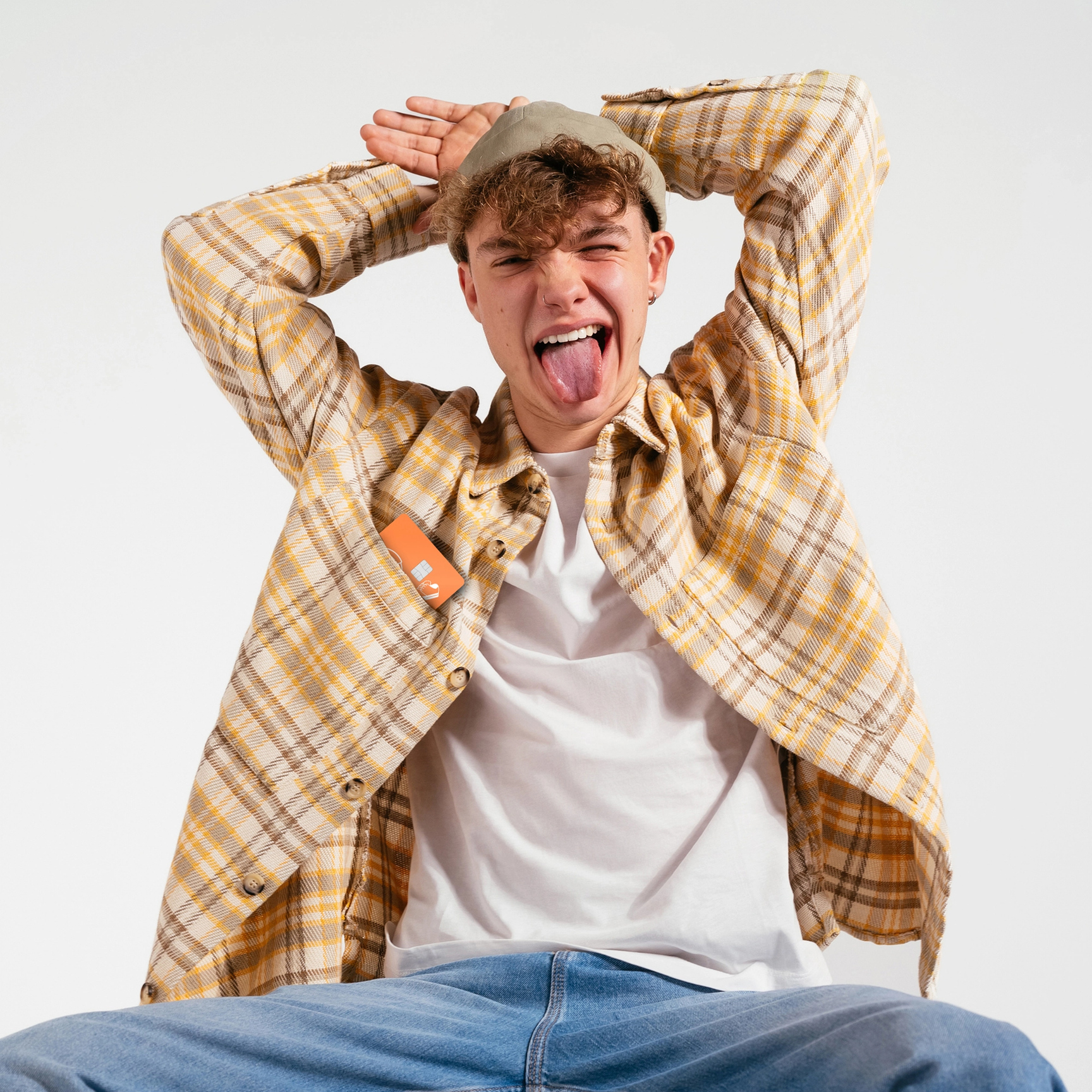 En tonåring i en gulrutig skjorta och mössa gör en lekfull min och räcker ut tungan mot kameran med händerna bakom huvudet.