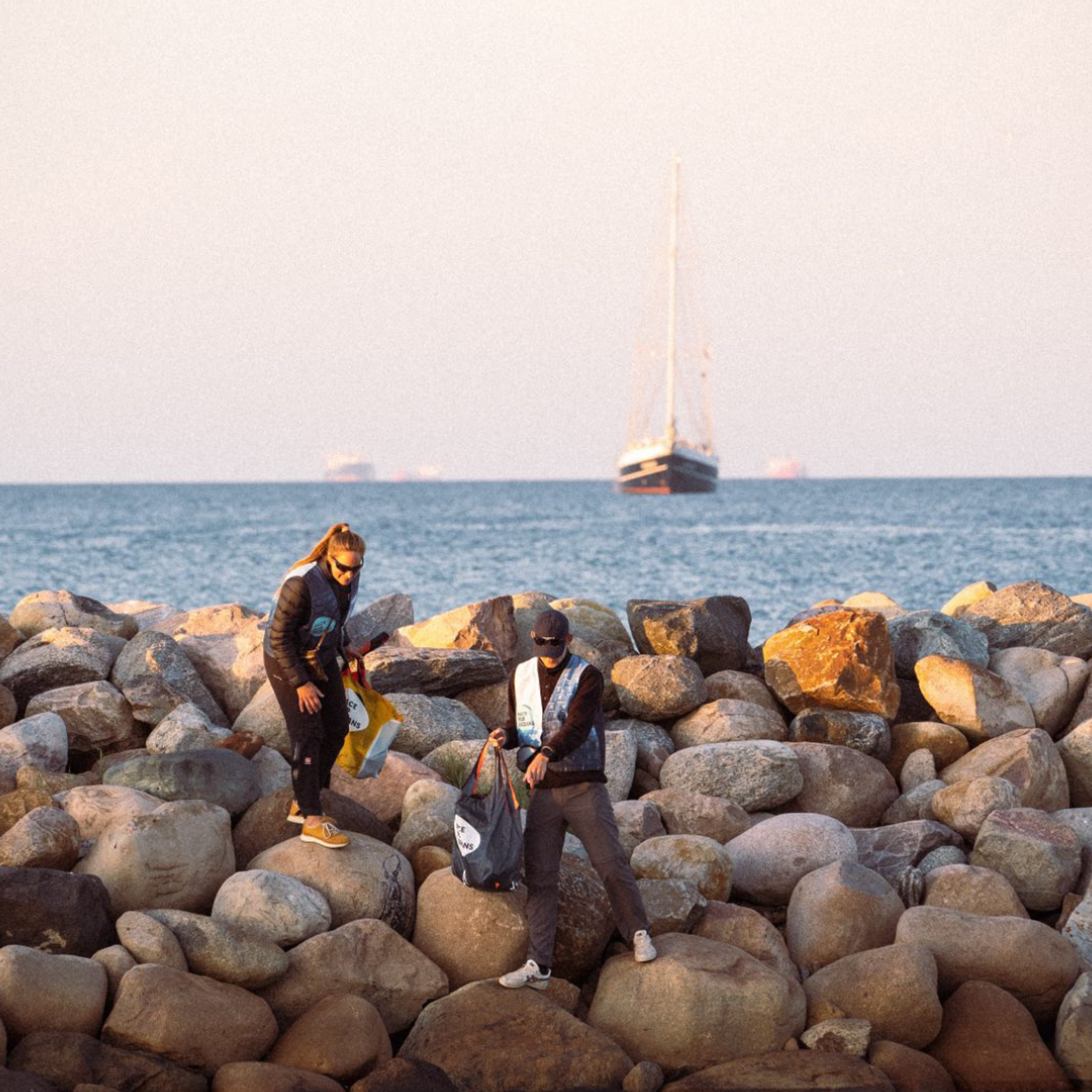 To frivillige samler søppel i en sekk mens de står på en steinete molo, som en del av et kystryddings-arrangement.