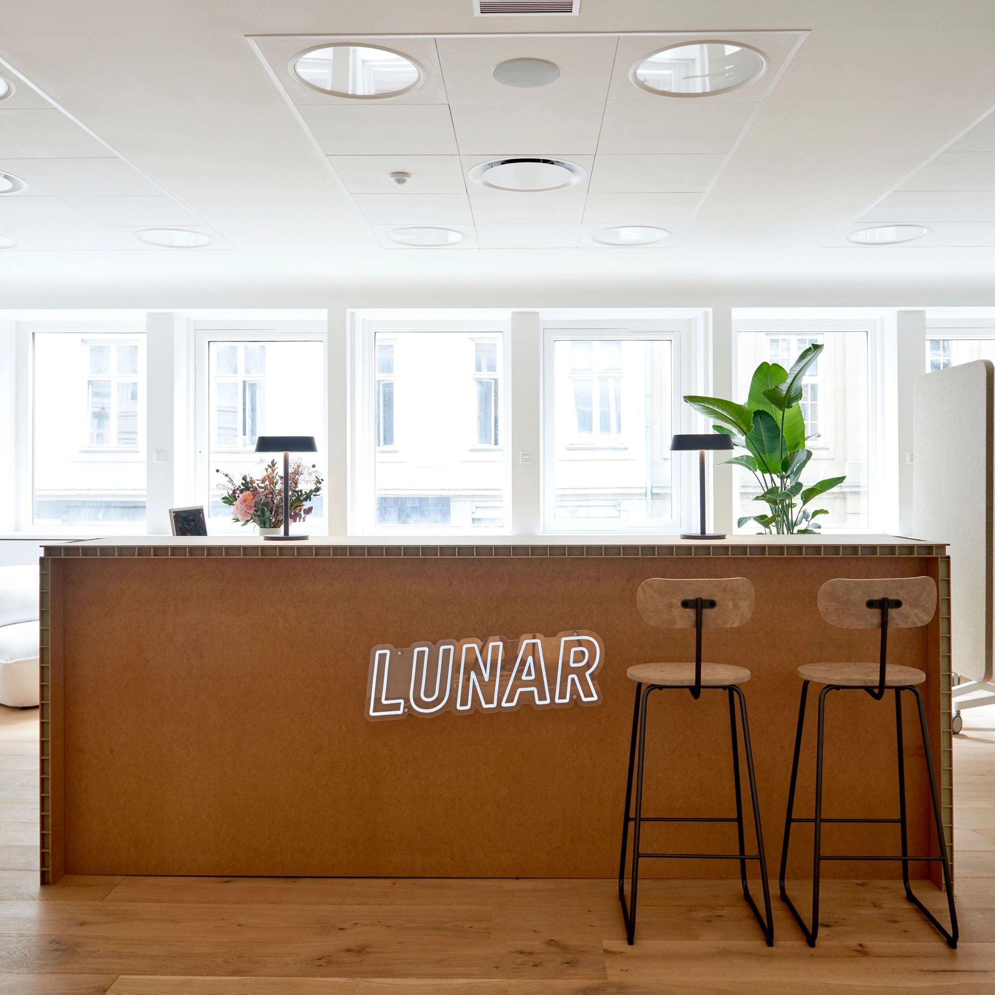 Det moderne og lyse resepsjonsområdet på Lunar-kontoret, med en treskranke som har et hvitt "LUNAR"-neonskilt på forsiden.