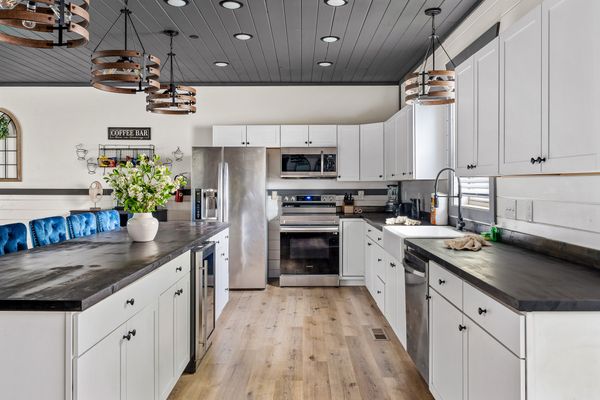 Modern kitchen with white cabinets, stainless steel appliances, black countertops, wooden floor, pendant lights, a vase of flowers on the island, and a Coffee Bar sign on the back wall—this inviting space blends contemporary elegance with the cozy charm often found in Smoky Mountain Cabin communities.