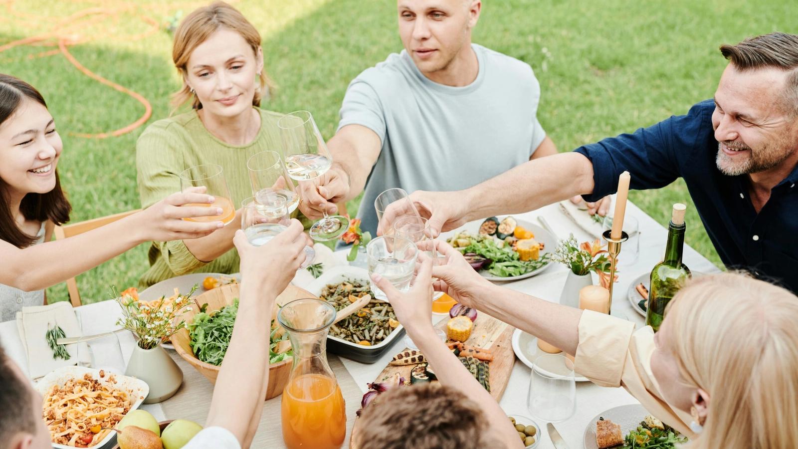 A group of people sitting around an outdoor table on a grassy lawn near Gatlinburg, raising their glasses for a toast. The table is filled with dishes and drinks, perfect after exploring Smoky Mountain waterfalls or hikes near Gatlinburg.