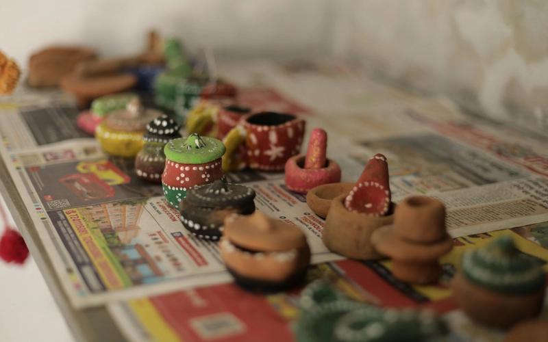 Small, hand-painted clay pots and vessels—showcasing the creativity of local crafts—sit atop colorful newspapers, arranged in rows. Each unique pot features vibrant colors and patterns, capturing the spirit of Gatlinburg Arts & Crafts handmade shops.