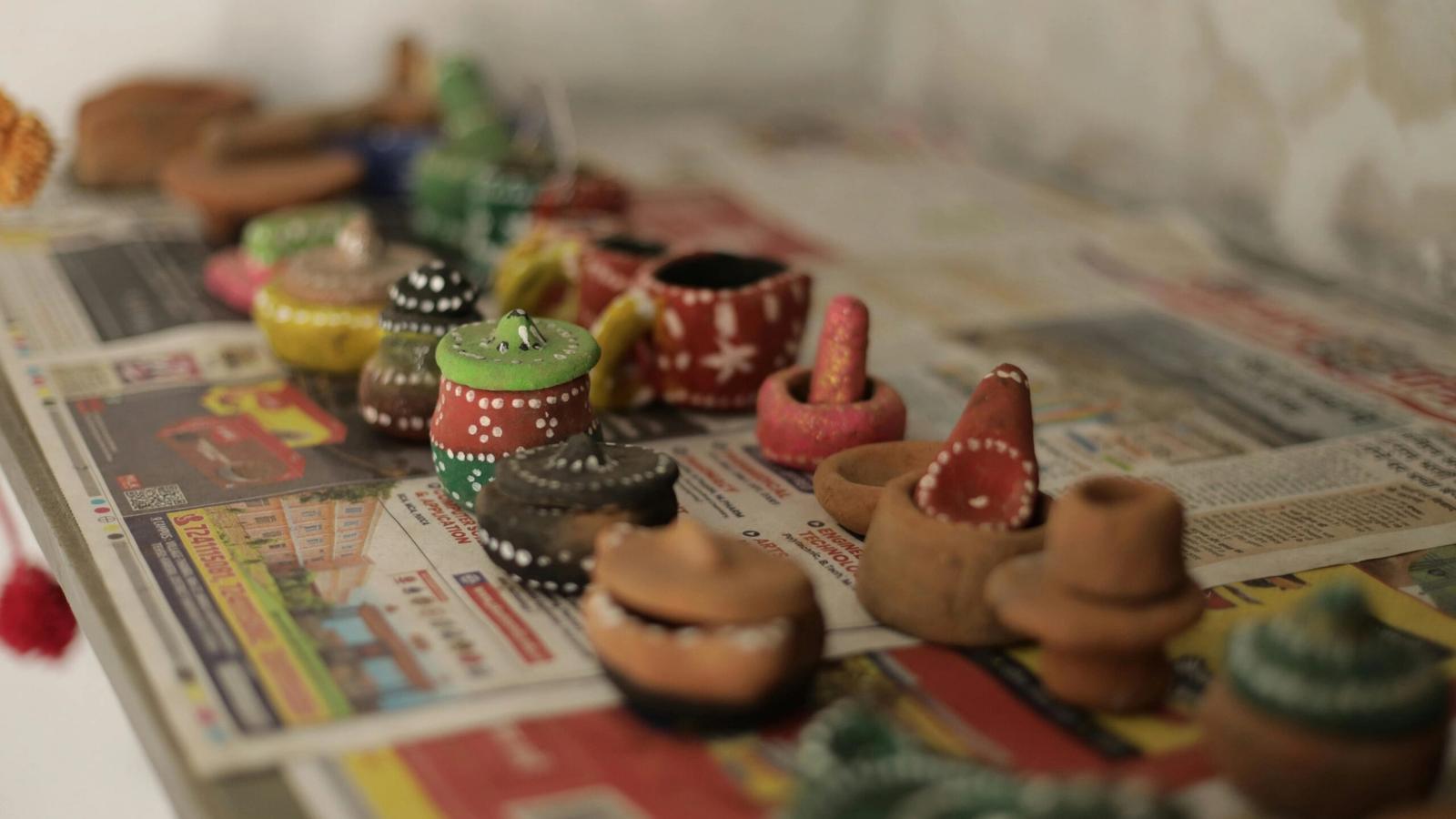 Small, hand-painted clay pots and vessels—showcasing the creativity of local crafts—sit atop colorful newspapers, arranged in rows. Each unique pot features vibrant colors and patterns, capturing the spirit of Gatlinburg Arts & Crafts handmade shops.